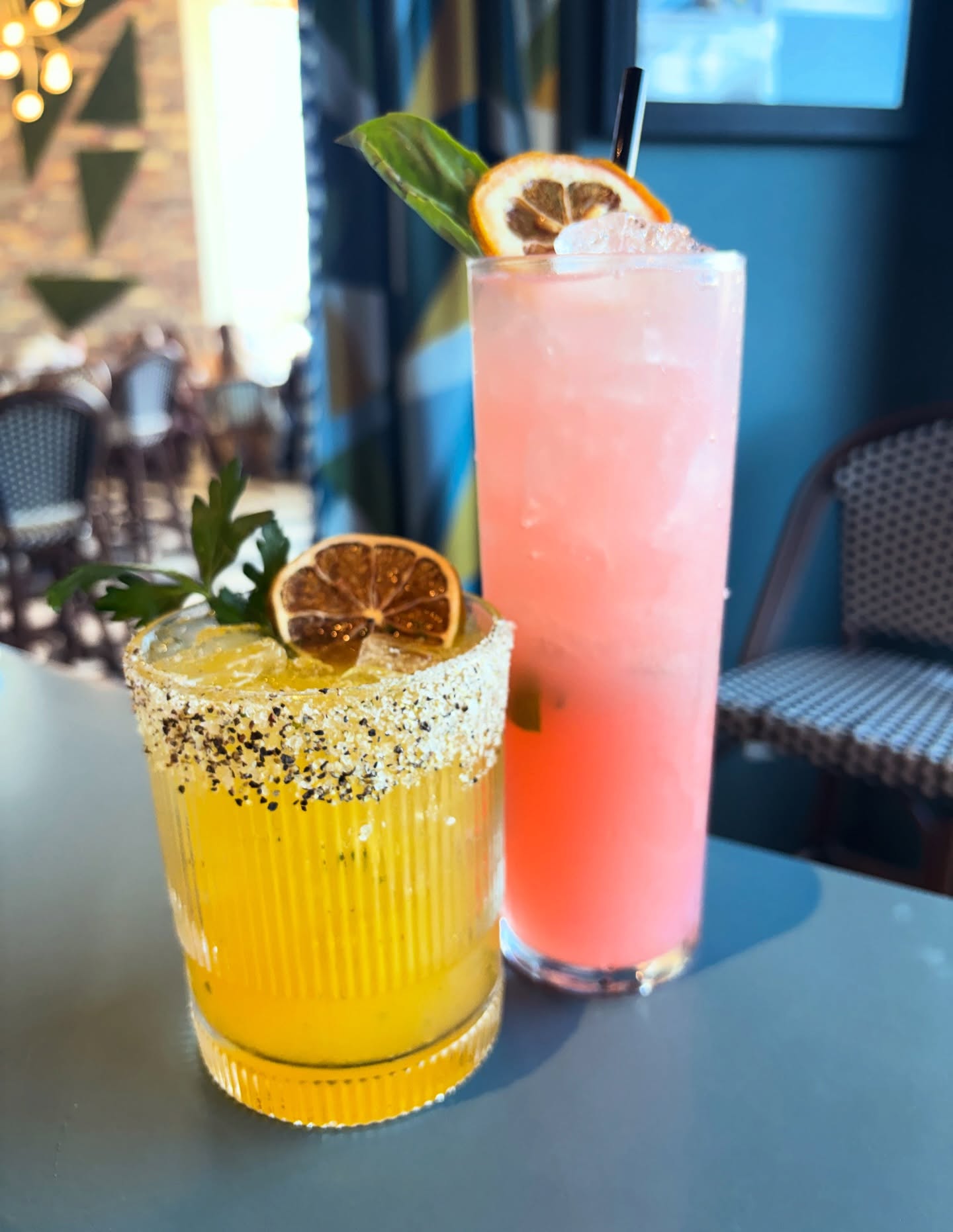 A salted yellow cocktail and a tall pink cocktail on a table at Candle Bar